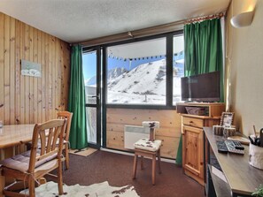 A cozy room with a wooden interior, a dining table with chairs, a television, and a view of a snowy mountain. - Studio Cabin in Aime 2000, 4 Pers, Sunny View (Plagne Aime 2000)