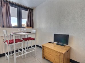A small room with a dining table set for two, a television on a wooden cabinet, and a window with curtains. - Studio for 2 at the foot of the slopes, Plagne Centre (La Plagne)