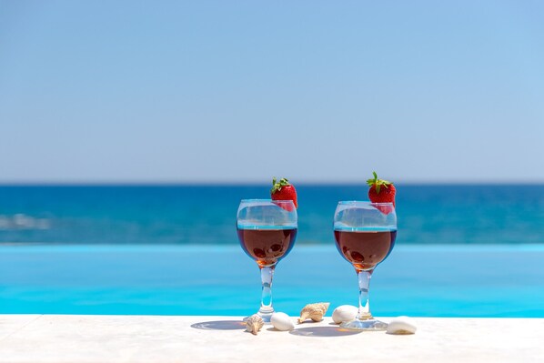 Two glasses of red wine with strawberries on a white surface by a pool with a clear blue sky. - Mary Beach 3 Villa (Sfakia)