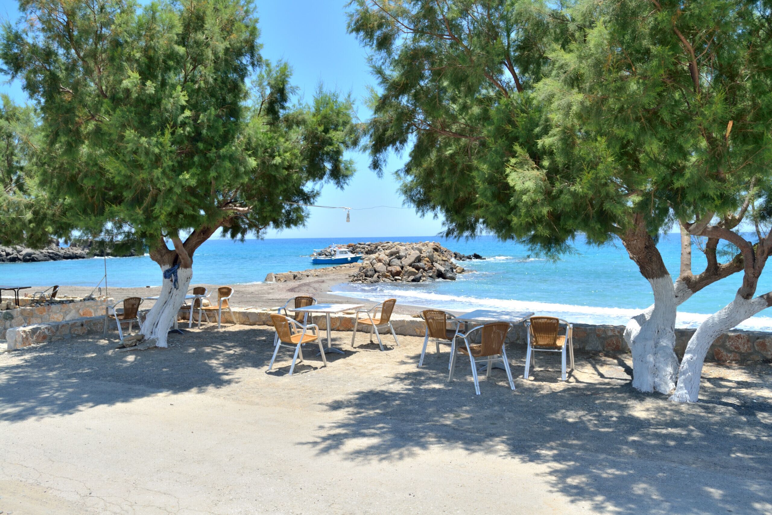 A beachside seating area with chairs and tables, overlooking the sea and rocky shoreline.