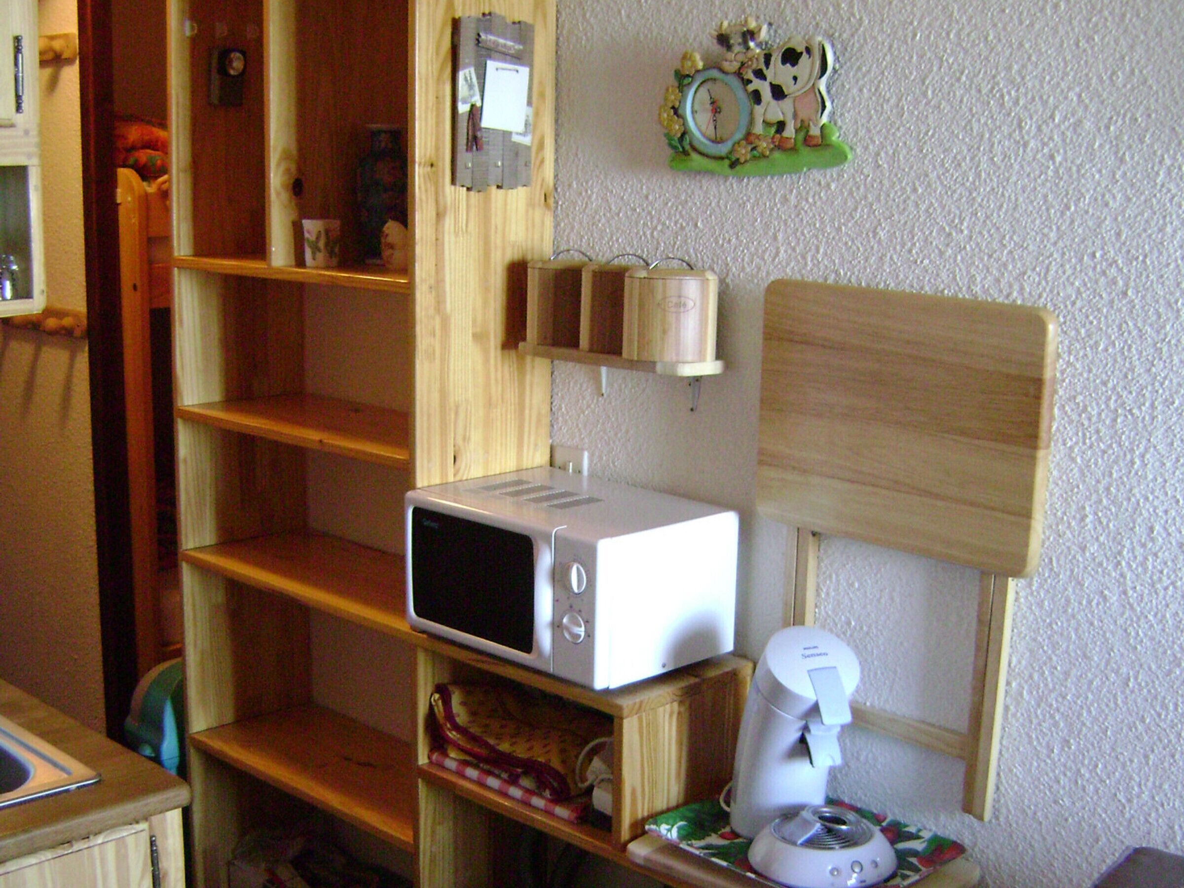 A kitchen with a microwave, toaster, and coffee maker on wooden shelves.