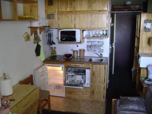 A compact kitchen with wooden cabinets, a microwave, a sink, and a refrigerator. - Cozy Studio in Samoëns - Perfect for 4 Guests (Samoëns)