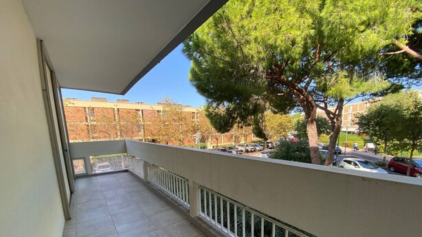 Un balcon doté d’un sol carrelé, d’une balustrade blanche et offrant une vue sur les voitures garées et les arbres.