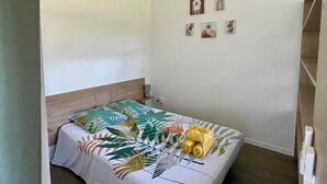 Ein Einzelbett mit Bettdecke mit tropischem Blattmuster, einem Holzkopfstück und einem Paar zusammengerollter Handtücher auf dem Bett.