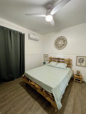 Ein Schlafzimmer mit einem Bett, einem Deckenventilator, einer Klimaanlage, einer Wanduhr und einem gerahmten Bild.