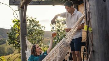 A hammock under a wooden pergola with a person standing and pouring a drink into a glass.
