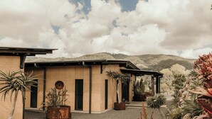 A modern building with a patio area, surrounded by various potted plants and a mountainous backdrop. - Mayan Farm Villas (Kin Kin)