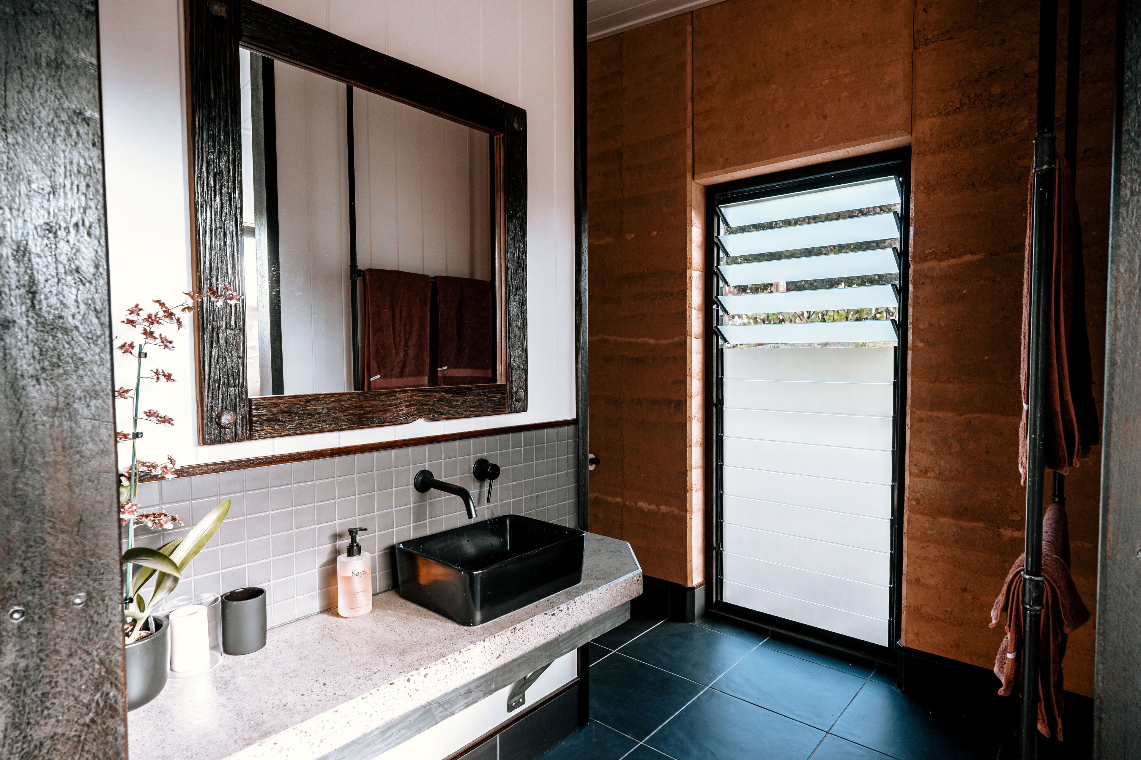 A bathroom with a black sink, white tiles, a mirror, and a towel rack.