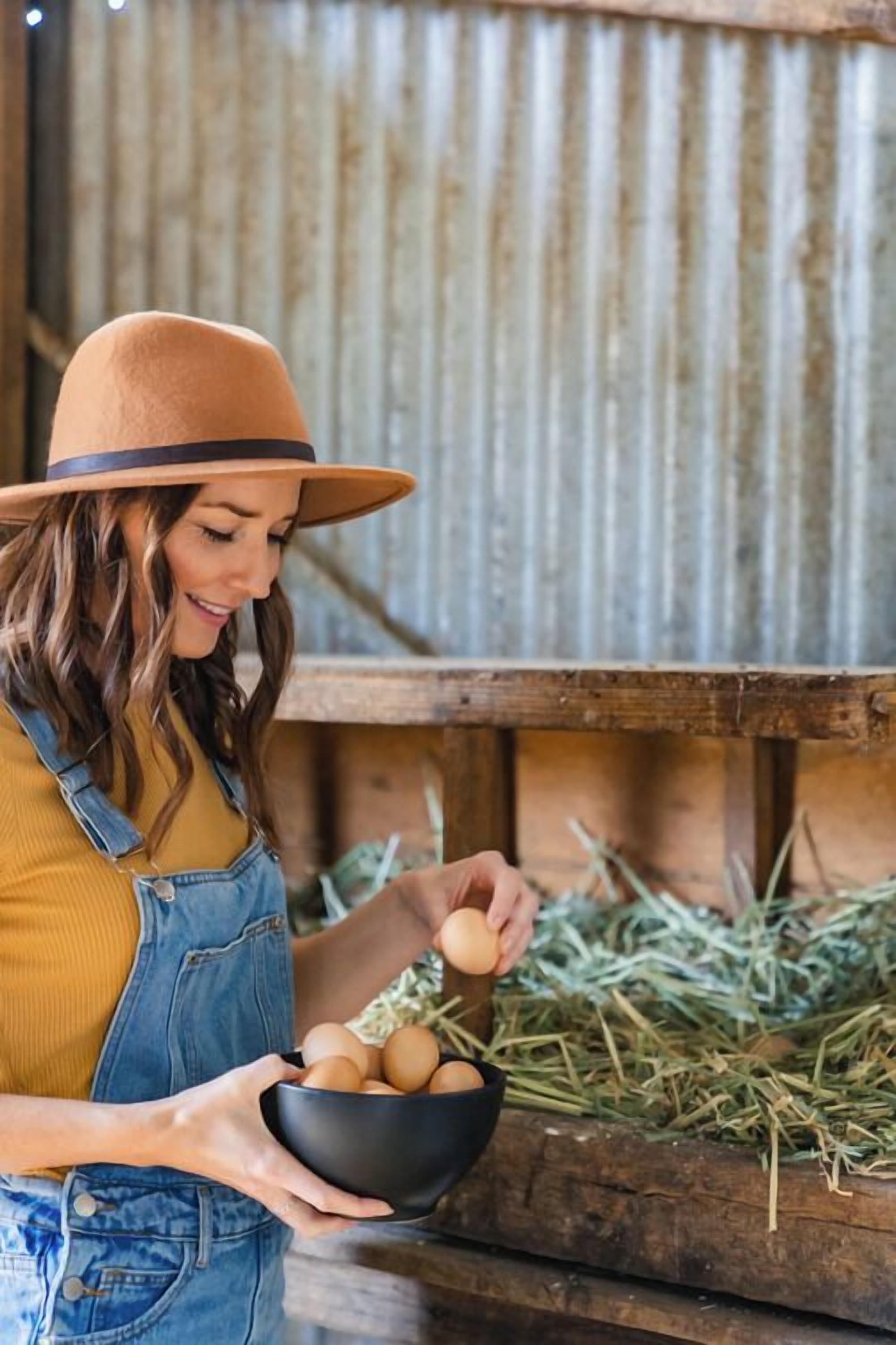 A person holding a bowl of eggs in a rustic setting with wooden structures and hay.