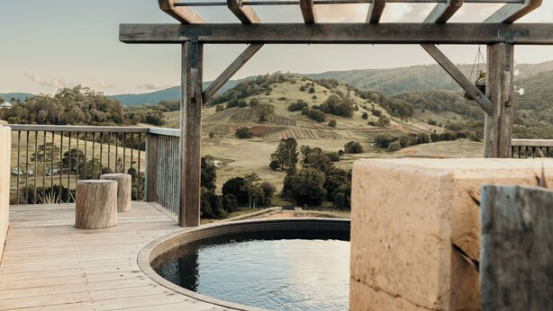A wooden deck with a pergola, a circular pool, and a view of rolling hills. - Mayan Farm Villas (Kin Kin)