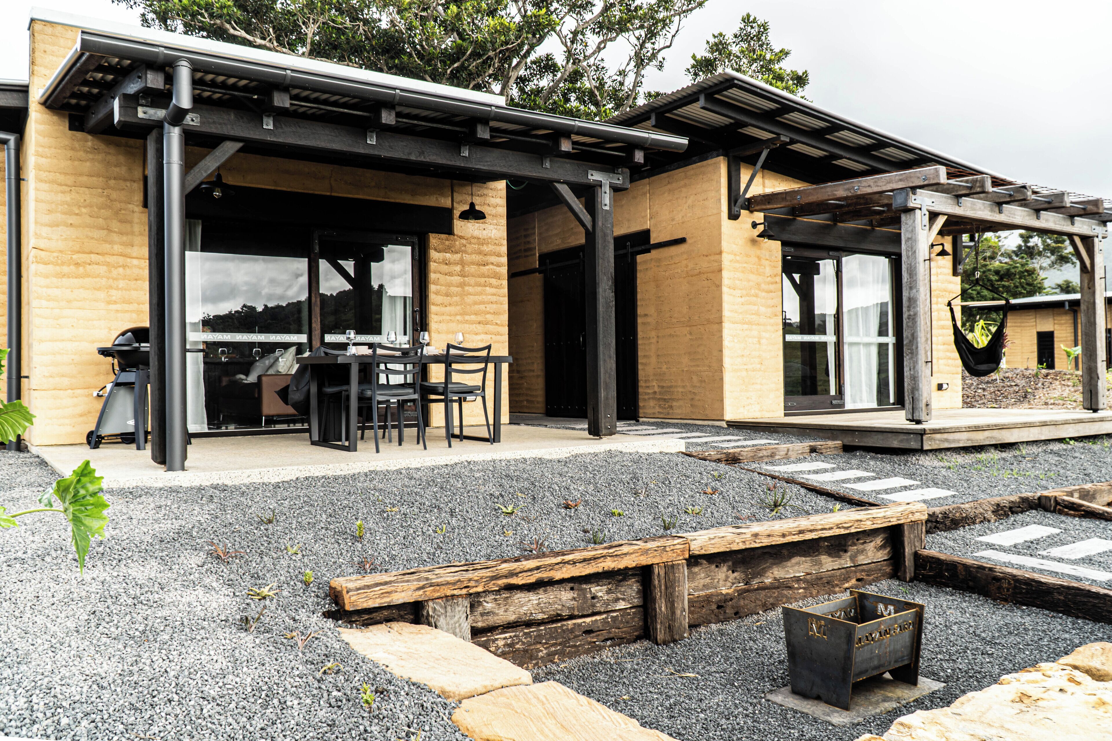 Una casa moderna con patio que incluye una mesa de comedor, sillas, una parrilla y una pérgola.
