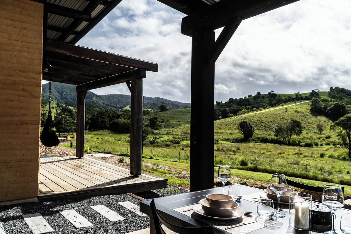 An outdoor dining area with a table set for two, overlooking a grassy hillside.