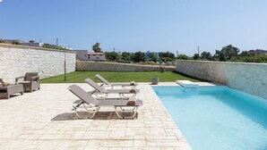 Uma área à beira da piscina com espreguiçadeiras, um muro de pedra e vista para a paisagem ao redor.