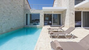 Área junto à piscina com espreguiçadeiras, um muro de pedra e uma porta de vidro que dá para um quarto.