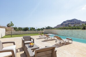 A poolside area with wicker furniture, a fruit bowl, and a view of a mountain. - Mythos 3 (Agios Vasileios)