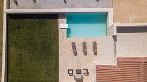 Oversigtsbillede af et poolområde med et afsondret loungeområde, en lille have og en fliseterrasse.