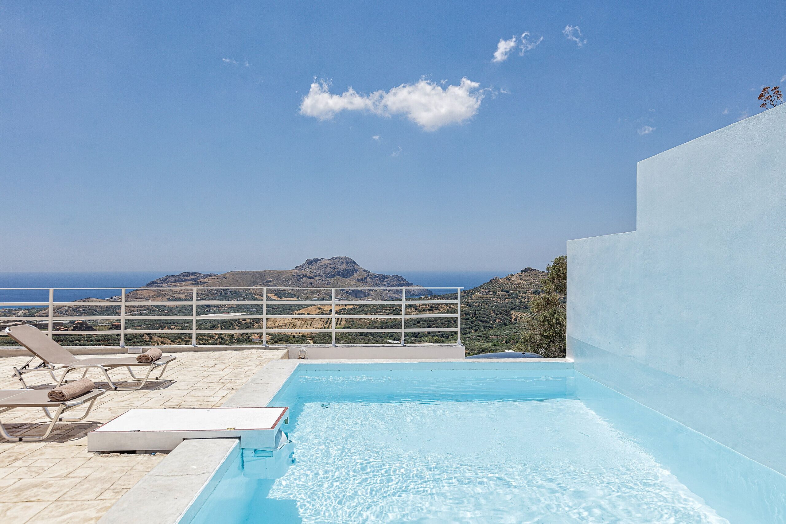 A pool area with lounge chairs and a view of the ocean.