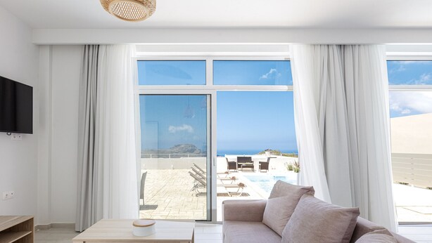 A modern living room with a sofa, a coffee table, and a TV mounted on the wall. - Petres Villas (Agios Vasileios)