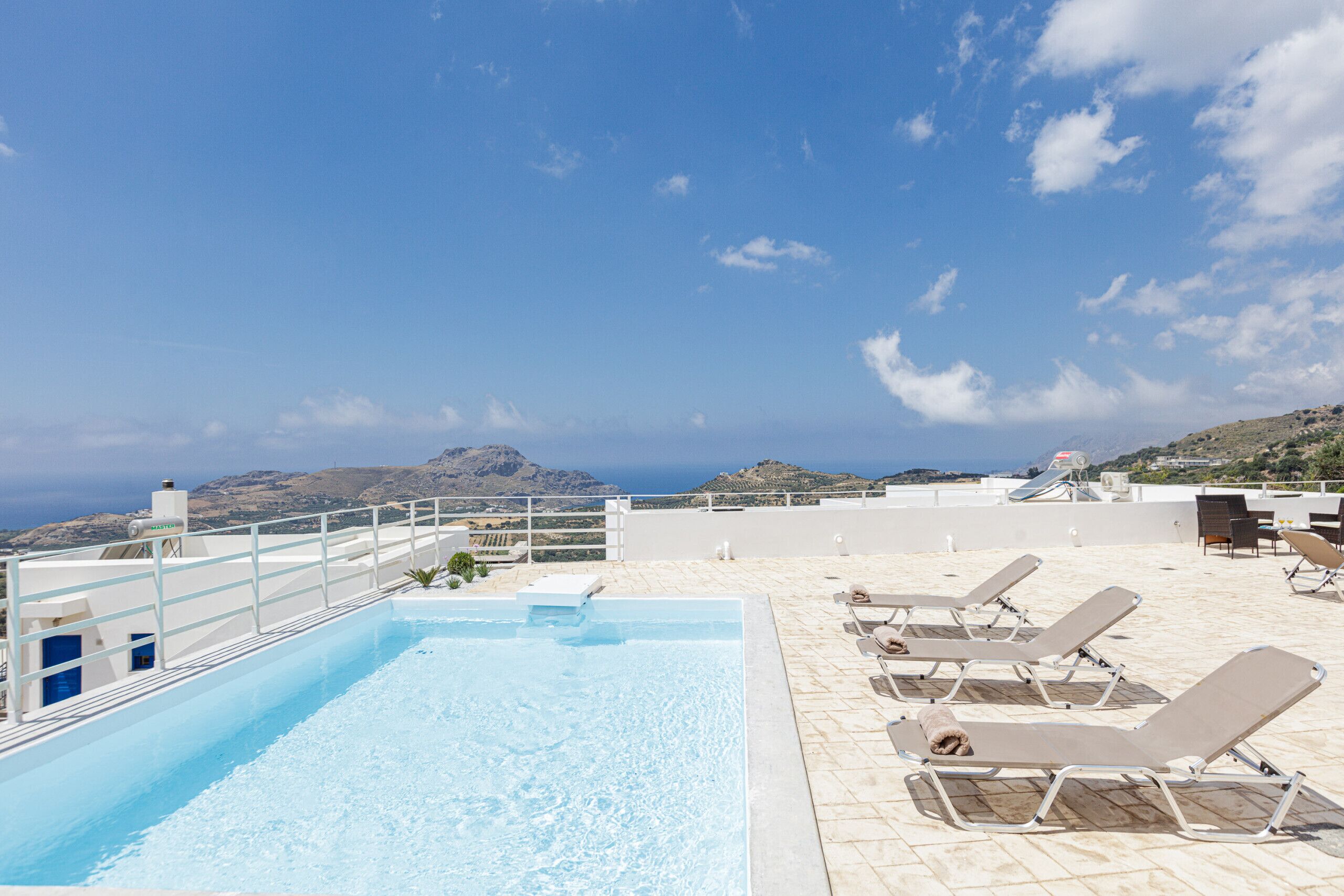 Une piscine sur le toit, avec une eau d’un bleu cristallin, entourée de chaises longues et offrant une vue panoramique sur l’océan et les collines.