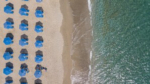 An aerial view of a beach with rows of blue umbrellas and beach chairs. - Petres Villas (Agios Vasileios)