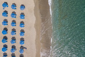 An aerial view of a beach with rows of blue umbrellas and beach chairs. - Petres Villas (Agios Vasileios)