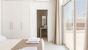 A hotel room with a bed, a wardrobe, a bathroom, and a large window. - Petres Villas (Agios Vasileios)