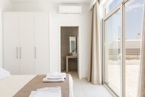 A hotel room with a bed, a wardrobe, a bathroom, and a large window. - Petres Villas (Agios Vasileios)