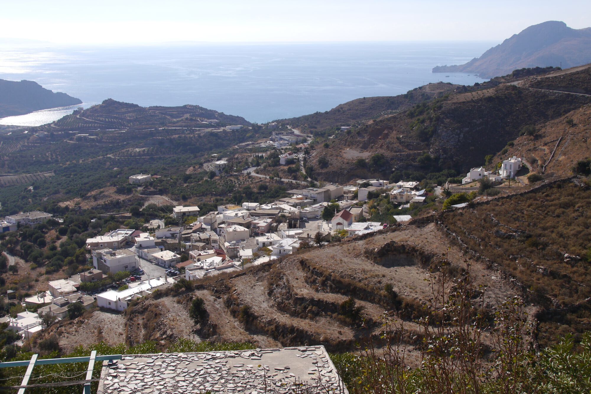 A coastal village with buildings nestled in hilly terrain, overlooking the sea.