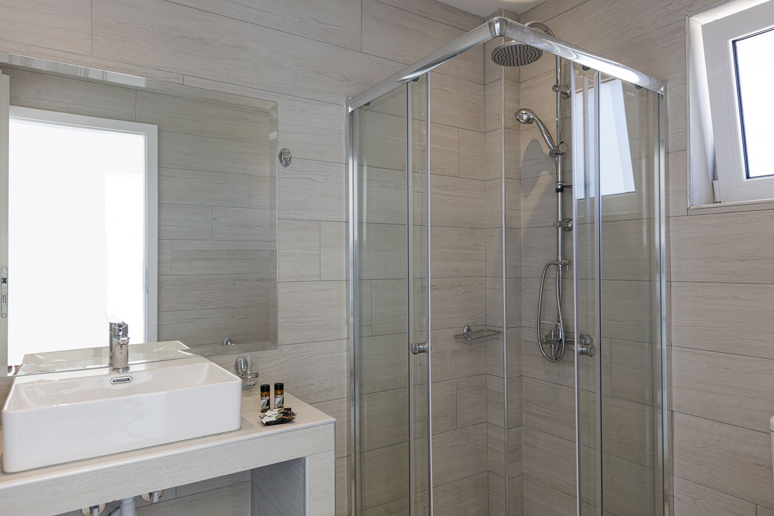 A modern bathroom with a glass-enclosed shower, a white sink, and a large mirror.