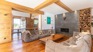 A modern living room with a wooden floor, a stone fireplace, and a large sectional sofa. - Chalet in the heart of the Pyrenees, at the foot of the slopes (Saint-Lary-Soulan)