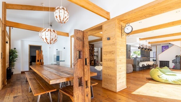 A spacious dining area with a wooden table and benches, a large wooden beam structure, and hanging spherical light fixtures. - Chalet in the heart of the Pyrenees, at the foot of the slopes (Saint-Lary-Soulan)