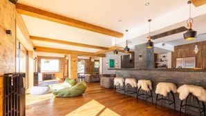 A spacious living area with wooden floors, a stone accent wall, and a bar with stools. - Chalet in the heart of the Pyrenees, at the foot of the slopes (Saint-Lary-Soulan)