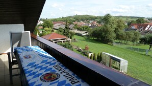 Un balcón con una mesa cubierta por un mantel a cuadros, con vistas a una zona residencial con casas y vegetación.