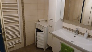 Un baño con lavamanos blanco, espejo y perchero.