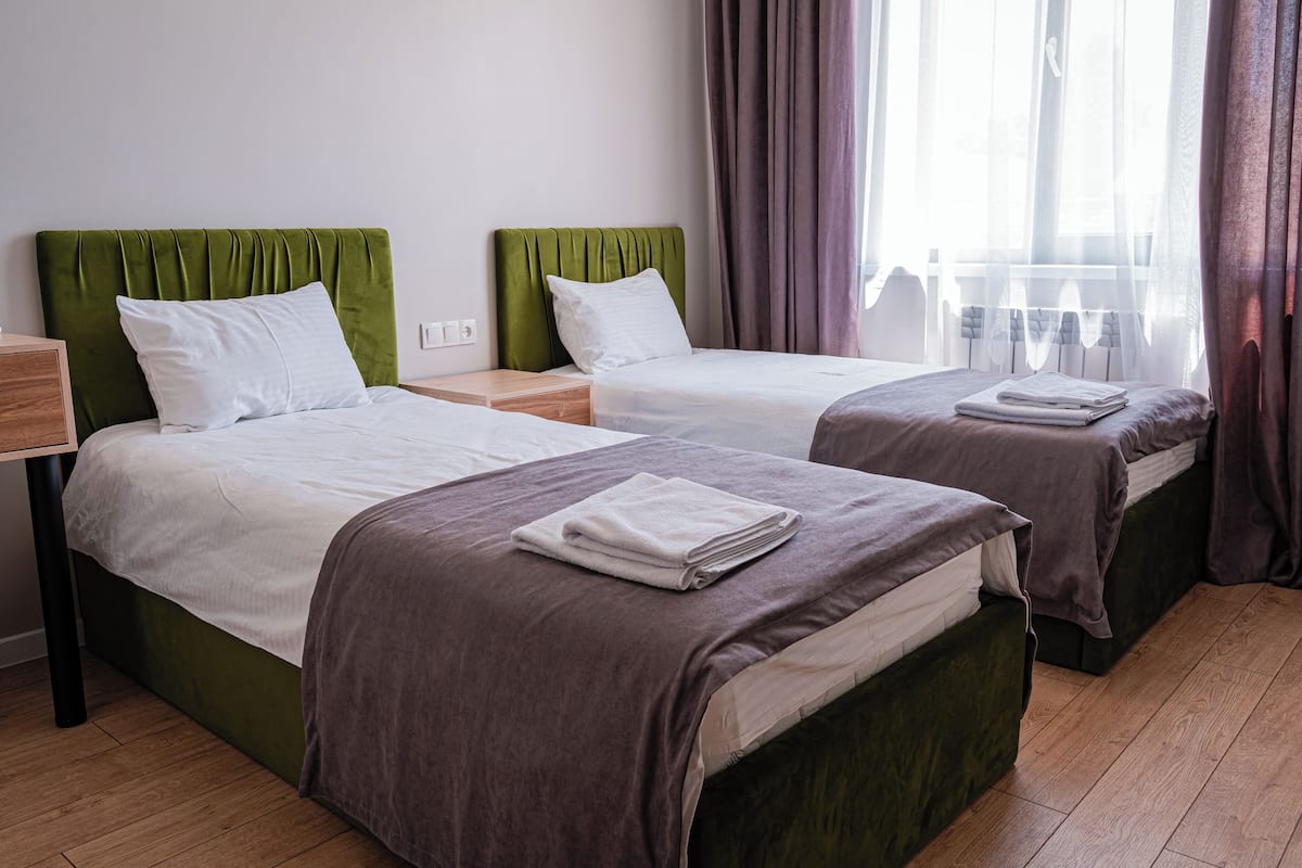 A hotel room with two beds, each with a green headboard, white bedding, and a folded towel on the bed.