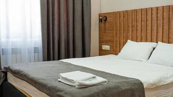 A hotel room with a wooden headboard, a bed with white linens, a grey blanket, and a grey curtain.