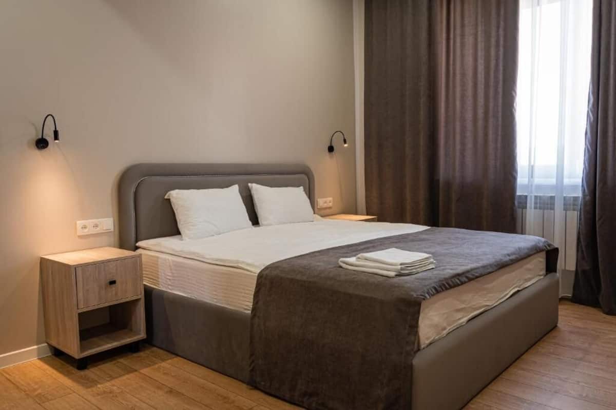A modern hotel room with a large bed, bedside tables, and a window with curtains.