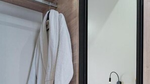 A modern bathroom with a wooden vanity, a towel rack with two white robes, and a mirror with a black frame. - BnB Hotel Shymkent (Shymkent)