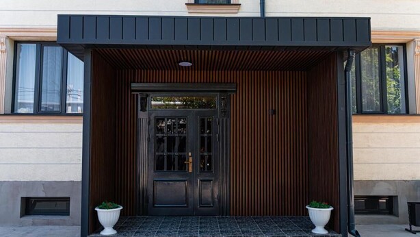 A modern building entrance with a black door, wooden slats, and two white planters. - BnB Hotel Shymkent (Shymkent)