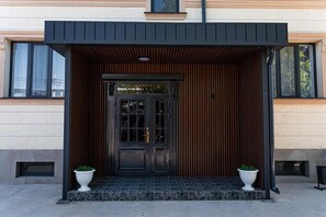 A modern building entrance with a black door, wooden slats, and two white planters. - BnB Hotel Shymkent (Shymkent)