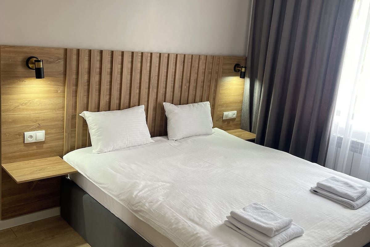 A hotel room with a large bed, wooden headboard, bedside tables, and a window with curtains.