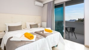 A hotel room with two beds, a balcony with a chair, and a view of the landscape. - Sunset Maisonettes (Agios Vasileios)