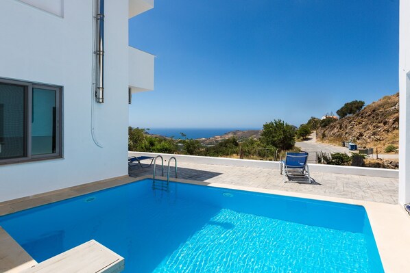 Ein Swimmingpool mit Meerblick, ein Stuhl und ein Gebäude mit einem Fenster.