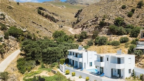 A modern two-story building with a swimming pool, surrounded by a mountainous landscape. - Sunset Maisonettes (Agios Vasileios)
