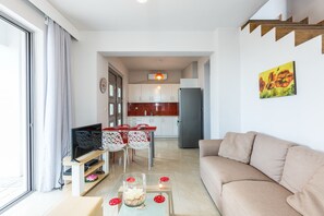Ein modernes Wohnzimmer mit einer Couch, einem Fernseher, einem Glastisch und einem Essbereich mit Stühlen und Tisch.