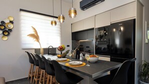 Een moderne keuken met een centraal eiland, zwarte barkrukken en een eettafel.