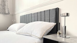 A modern hotel room with a large bed, grey upholstered headboard, and a bedside table with a lamp. - York City Centre Flat with view - Best Location - Walk to Everything (York)