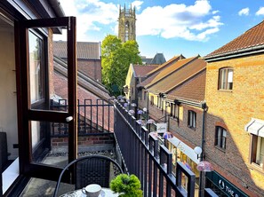 Un balcone con vista su un campanile, edifici in mattoni e una strada con ombrelloni.