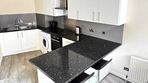 A modern kitchen with white cabinets, a black granite countertop, a built-in washing machine, and a coffee maker. - York City Centre Flat with view - Best Location - Walk to Everything (York)
