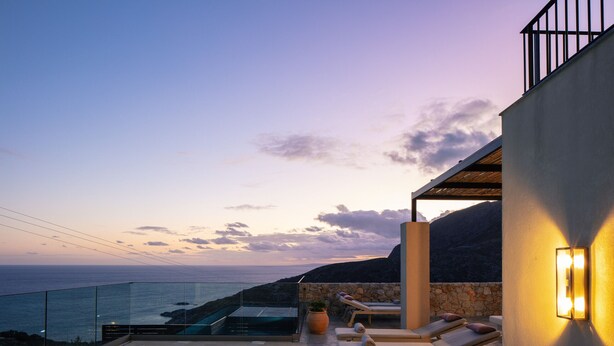 Een modern zwembad met ligbedden en een glazen balustrade met uitzicht op zee.